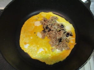溶き卵をフライパンに流し、なすとひき肉をのせて包む。
